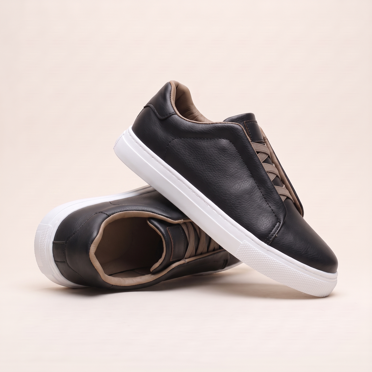 Black slip-on low-top sneakers angled to show the taupe elastic panel and white cupsole