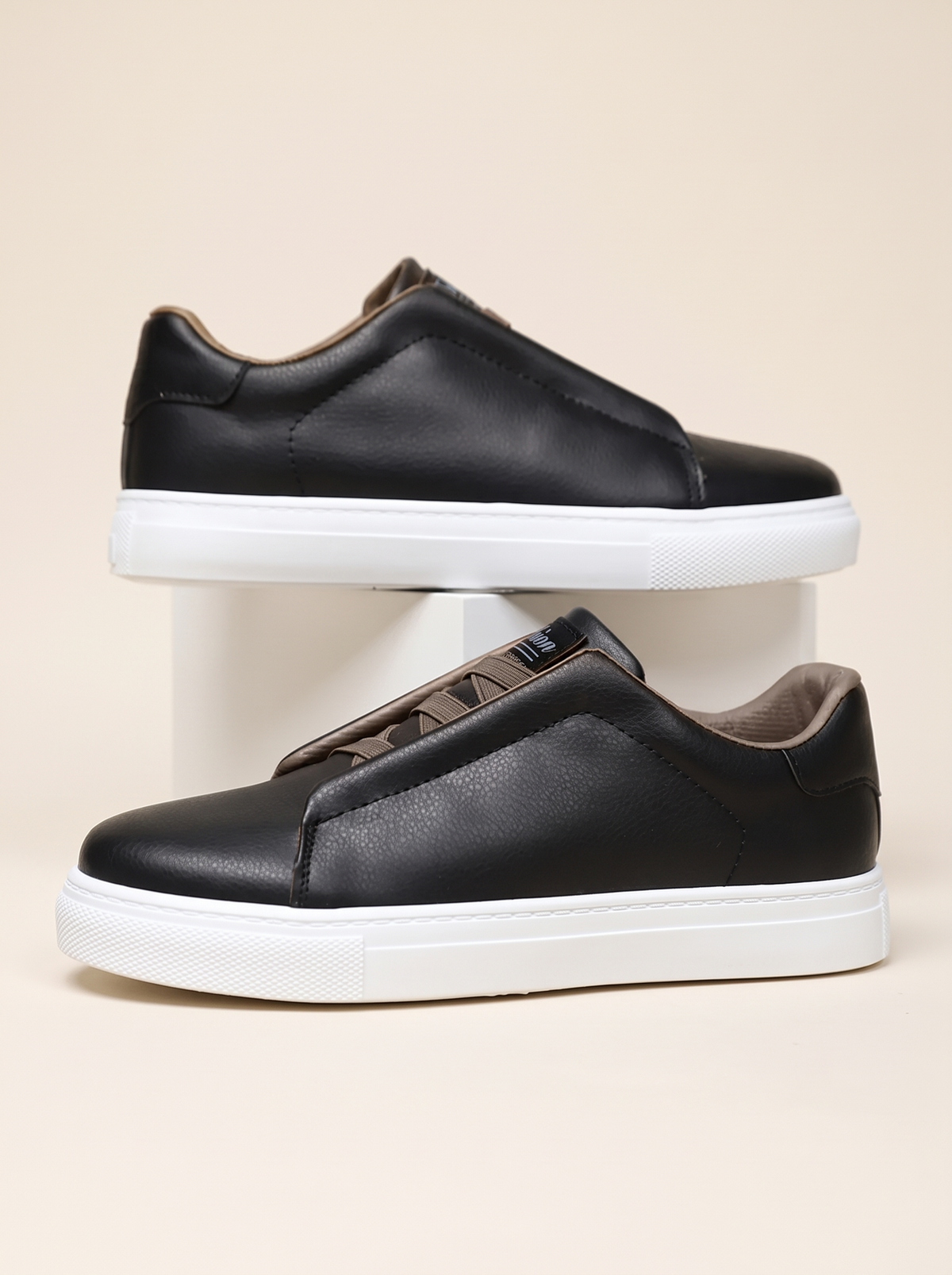 Pair of black slip-on low-top sneakers with taupe lining and white cupsole, side profile